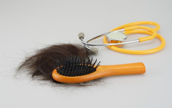 Wooden hair brush with lost brown hair and stethoscope on white background.