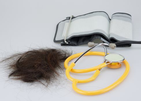 Group of brown lost hair placed near stethoscope and sphygmomanometer on white background.