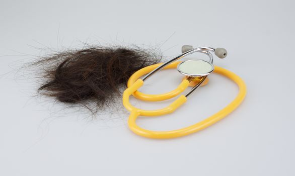 Group of brown lost hair placed near stethoscope on white background.