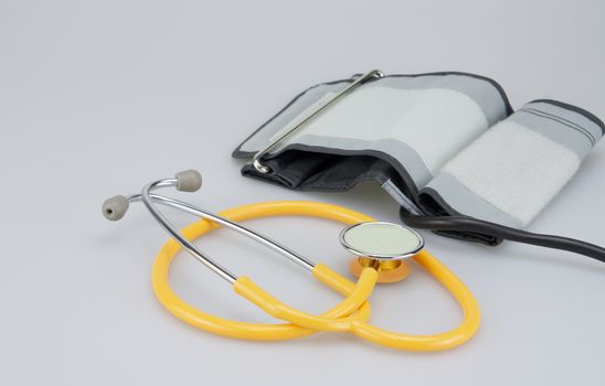 Yellow stethoscope and cuff of sphygmomanometer were placed on white background.