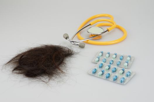 Brown lost hair with stethoscope and medicine placed on white background.