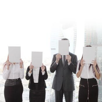 Portrait of business people group holding white papers and covering their faces