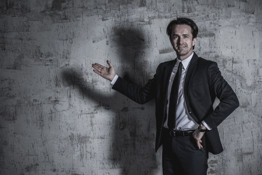 Portrait of a businessman in suit showing to empty space over concrete wall background