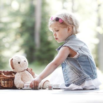 Pretty girl playing with teddy bear outdoors