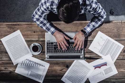 Businessman working on laptop with financial documents, top view