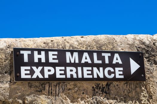 Board of the Malta Experience program - explaining the history of island Malta. Black board on the stone fence, bright blue sky.