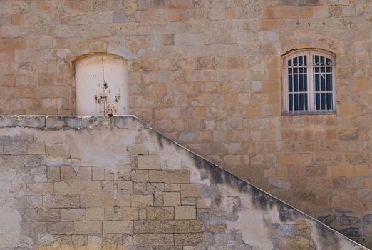 Old building made of stone bricks with a window and a gate. Line of the staircase. Capital of island Malta, Valletta.