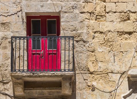 Old traditional building made of stone bricks with a balcony and a red door. Valletta, capital of island Malta.
