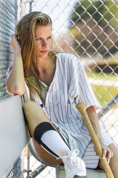 Blonde female model posing outdoors at a baseball diamond wearing baseball equipment.