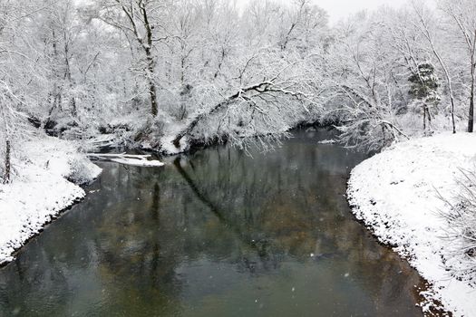 A winter landscape show snow falling on a creek with trees