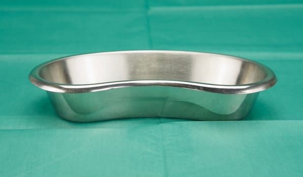 Kidney-shaped bowl, a stainless steel container, placed on green fabric in operation room.