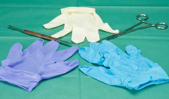 Surgical equipment and three pieces of gloves on green fabric.