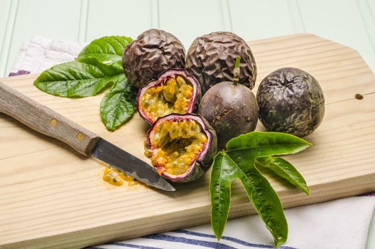 Passion fruits with leaves, knife and white flowers in jar on the vintage wooden table.