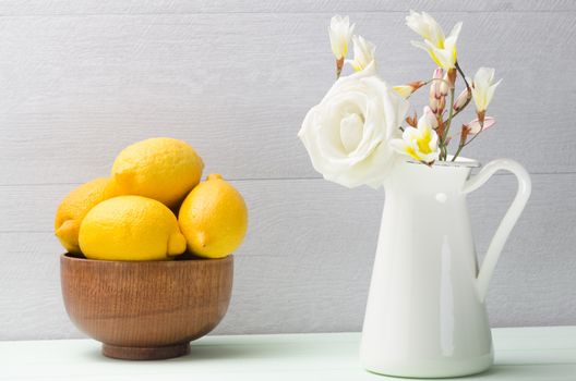 Wooden bowl with lemons and white flowers in jug.