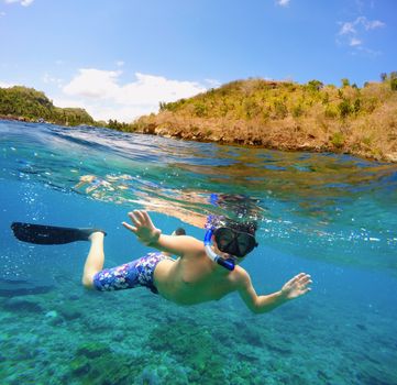 Underwater and surface split view in the tropics paradise with snorkeling boy fish and coral reef, above waterline, beautiful view on tropical island. Nusa Penida bali, Indonesia. Holiday vacation concept