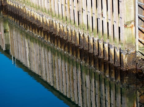 Wooden dock breakwall in a marina harbour with reflection in calm blue ocean sea