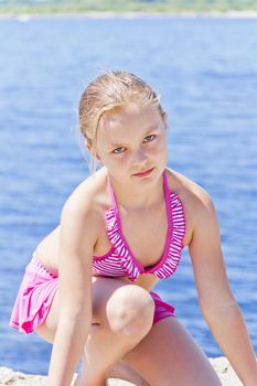 Cute angry girl on the riverbank in pink swimsuit