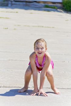 Cute jumping girl on the riverbank in pink swimsuit