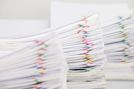 Pile overload paperwork of report with colorful paperclip have blur pile overload document as foreground and background place on white table.