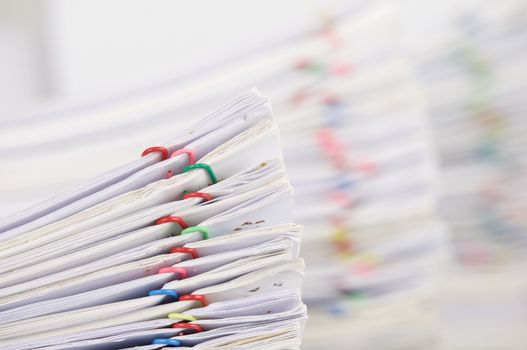 Pile overload paperwork of report with colorful paperclip have blur pile overload document as background place on white table.