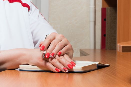 Female hands with manicure over pages of a notebook hold a pen