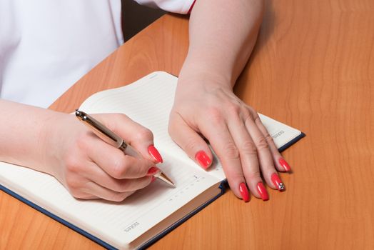 Female hands with manicure over pages of a notebook hold a pen