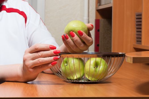 Female hands with manicure get green apples from a basket