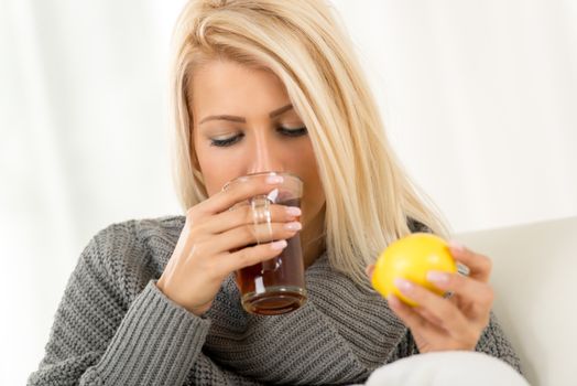 Cute blonde girl in a warm wool sweater drinking tea, while the other hand holds a lemon.