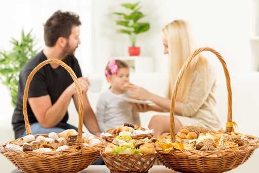 Beautifully decorated woven basket with pastries. In the background you can see a happy family, a father, mother and little daughter, enjoy the beautiful taste of baked goods.