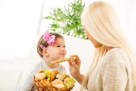 Mom and her cute little daughter sitting on the couch, holding a wicker basket  with pastry and offered her daughter.