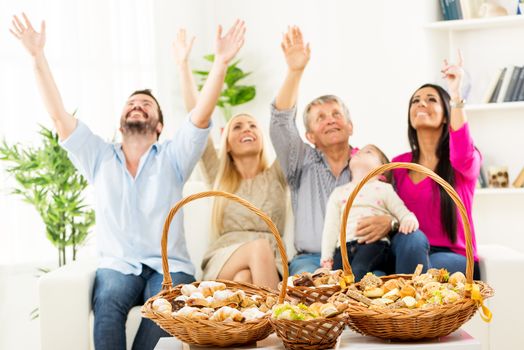 Woven baskets with nicely decorated cakes, standing on a table in the living room. In the background you can see a happy family sitting on the couch, arms raised looking up.