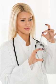 Pretty blonde young woman in a white coat, with a stethoscope over the neck preparing an injection, putting the needle on the syringe.