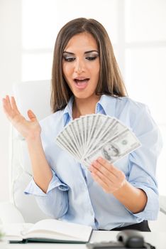 Young businesswoman holding money in hand and with an expression of surprise on her face looking into money.
