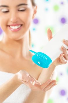 A young girl with a towel wrapped around her chest holds in her hand tube of body lotion and poured it on the other hand. The focus is on the hands and tube.
