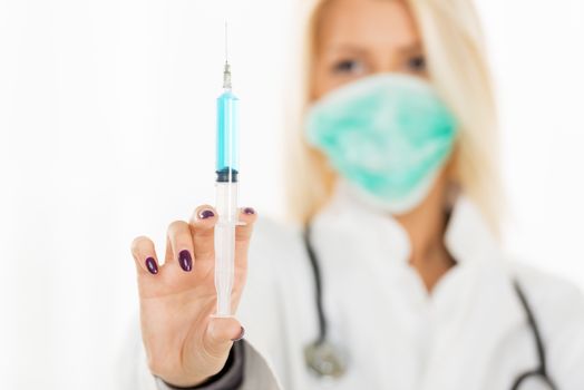 Close-up injections with blue liquid, in the hands of a pretty blonde nurse with surgical mask with face out of focus.