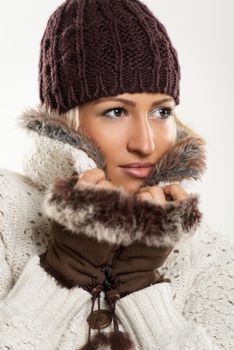 Beautiful young girl In winter clothes with a wool cap and fur gloves, sticks to the fur collar In which is tucking.