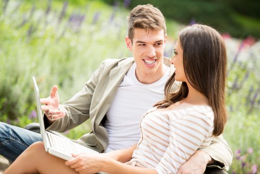 Young happiness couple sitting on bench and using laptop at park.