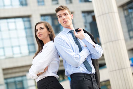 Young business couple standing in front of office building leaning back on each other.