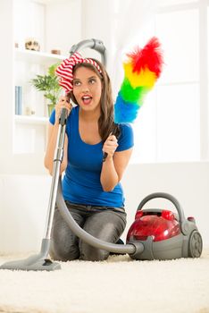 A young housewife kneeling beside the vacuum cleaner with duster in hand, satisfied with the good work cleaning up the house.