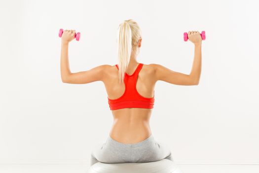 Cute sporty Young girl sitting to pilates ball and exercising with dumbbells. Rear view.