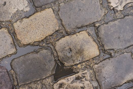 Water puddles from rain on wet cobblestone road 