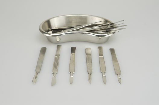 Many types of forceps and scalpel in kidney shape bowl on white background.