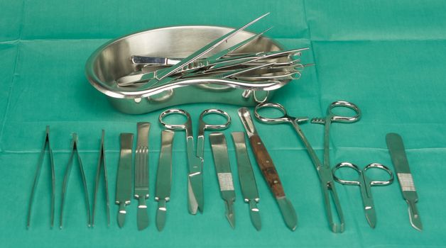 Medical instruments  and kidney shape bowl put on green fabric.