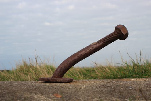 Bended rusty bolt in concrete with clouds