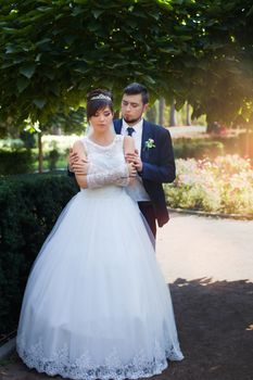 Happy smiling newlyweds walking outdoors, kissing and embracing on their wedding day