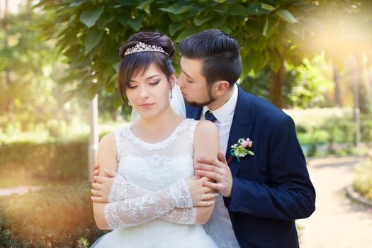 Happy smiling newlyweds walking outdoors, kissing and embracing on their wedding day