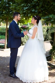 Happy smiling newlyweds walking outdoors, kissing and embracing on their wedding day