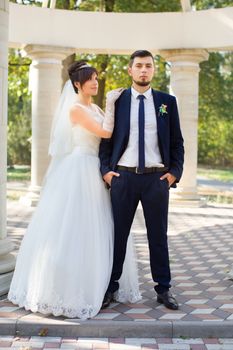 Happy smiling newlyweds walking outdoors, kissing and embracing on their wedding day