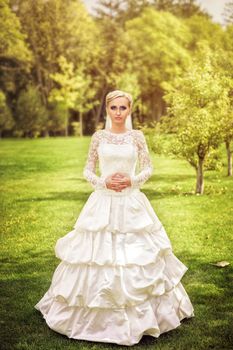 Beauty bride in bridal gown with bouquet and lace veil on the nature. Beautiful model girl in a white wedding dress. Female portrait in the park. Woman with hairstyle. Cute lady outdoors
