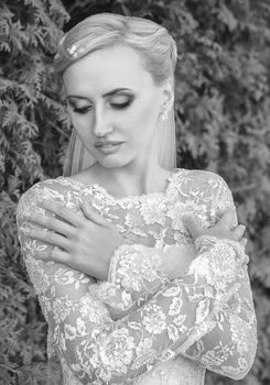 Beauty bride in bridal gown with bouquet and lace veil on the nature. Beautiful model girl in a white wedding dress. Female portrait in the park. Woman with hairstyle. Cute lady outdoors